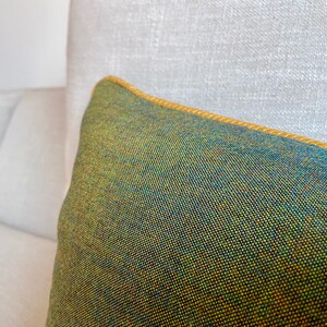 May include: A green and blue cushion with a yellow trim. The cushion is made of a textured fabric.