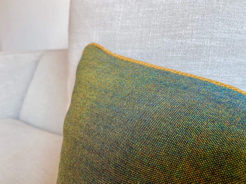 May include: A green and blue cushion with a yellow trim. The cushion is made of a textured fabric.