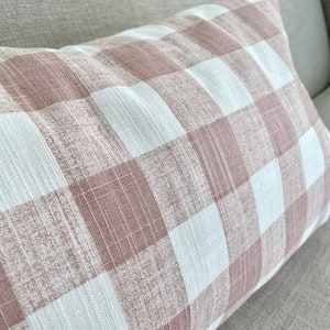 Op de afbeelding: Een roze en wit gingham kussen met een textuur. Het kussen ligt op een lichtbruine bank.