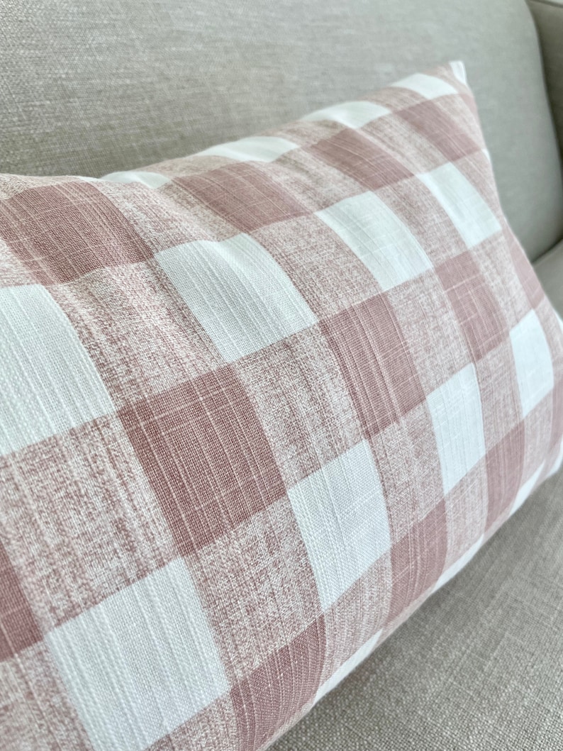 Op de afbeelding: Een roze en wit gingham kussen met een textuur. Het kussen ligt op een lichtbruine bank.