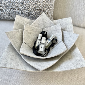 May include: A gray felt flower-shaped bowl with four small bottles inside. The bottles are clear glass with silver caps and black labels.