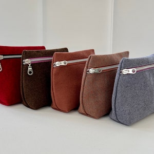 May include: Five zippered pouches in different colors: red, brown, orange, brown, and gray. The pouches are made of a soft, textured fabric and have a zipper closure.