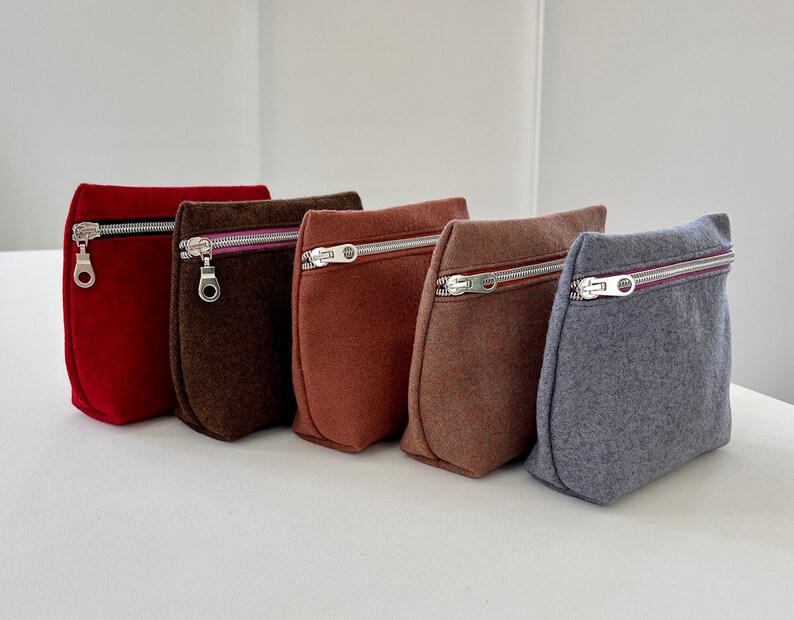 May include: Five zippered pouches in different colors: red, brown, orange, brown, and gray. The pouches are made of a soft, textured fabric and have a zipper closure.