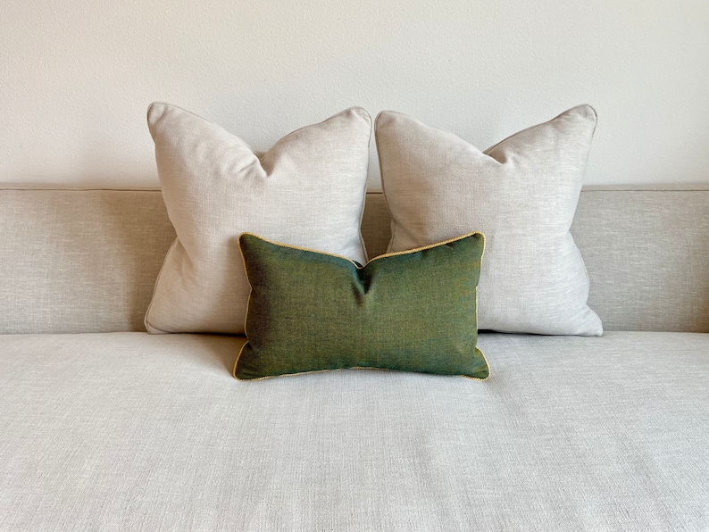 May include: Two light beige throw pillows with a dark green throw pillow in the centre. The pillows are on a light beige sofa.