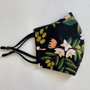 May include: Black face mask with a floral pattern featuring white and pink flowers and green leaves.