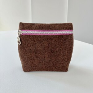 May include: A brown felt zippered pouch with a pink zipper pull. The pouch is sitting on a white surface.
