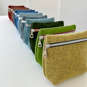 May include: A row of felt zipper pouches in various colors, including red, blue, green, and yellow. The pouches are lined up in a row, with the yellow pouch in the foreground.