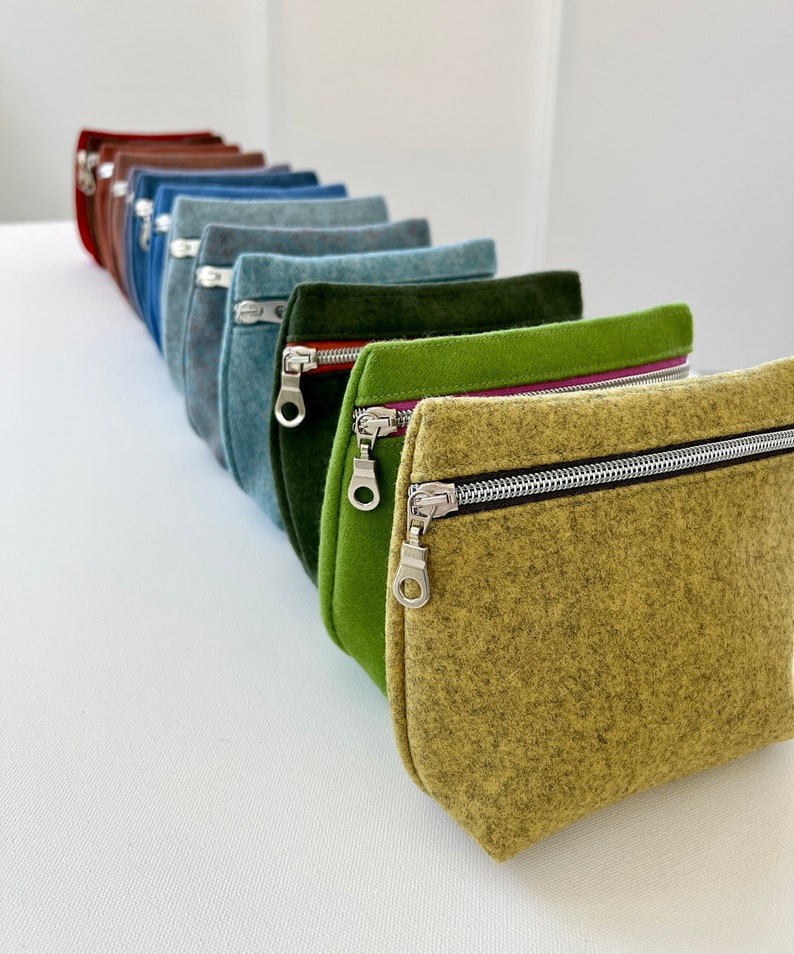 May include: A row of felt zipper pouches in various colors, including red, blue, green, and yellow. The pouches are lined up in a row, with the yellow pouch in the foreground.