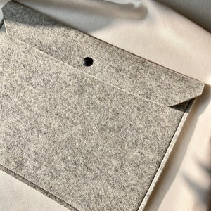 Puede incluir: Una funda para portátil de fieltro gris con cierre de botón negro.