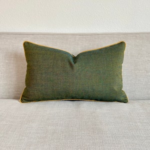 May include: A dark green cushion with a gold trim. The cushion is sitting on a light grey sofa.