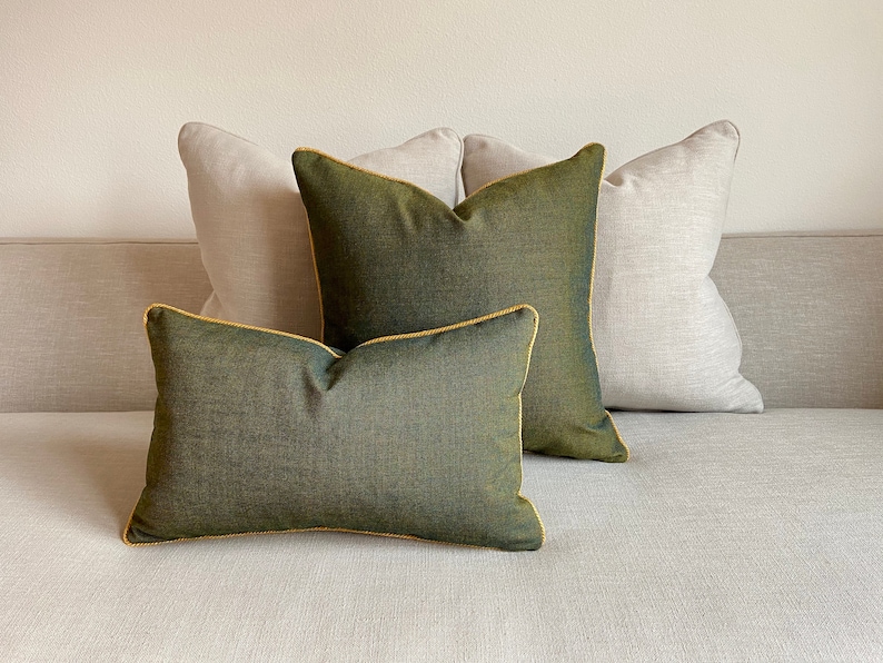 May include: Three decorative throw pillows on a light beige sofa. Two pillows are a light beige linen fabric and one pillow is a dark green fabric with a yellow trim.