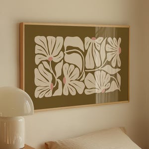 May include: A framed floral art print with a wooden frame. The artwork features a repeating pattern of white flowers with pink centers on an olive green background. A white mushroom lamp sits on a wooden dresser.