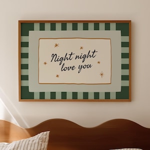 以下が含まれることがあります： 寝室に飾られた「Night night love you」の文字が入った額入りのプリント。 アートワークは、薄緑色と茶色のボーダーとクリーム色の背景です。 ベッドにはストライプの寝具と木製のヘッドボードがあります。