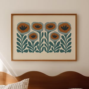 May include: A framed floral art print featuring stylized flowers in shades of orange, blue, and green. The artwork is displayed above a bed with striped bedding and a wooden headboard. The overall aesthetic is minimalist and modern.