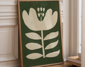 May include: A framed art print featuring a large, stylized white flower against a dark green background. The flower has a detailed center and is set in a natural wood frame. The artwork is leaning against a white wall and wooden floor.