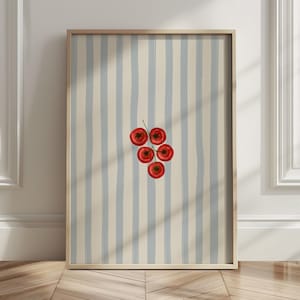 May include: A framed art print showing five red tomatoes on a green stem. The background has vertical stripes of light blue and beige. The frame is a light brown colour.