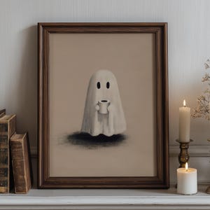 May include: A framed print featuring a whimsical ghost holding a coffee cup. The artwork is set against a neutral background and framed in dark wood. The scene is complemented by lit candles in ornate holders, creating a cozy, Halloween-themed aesthetic.