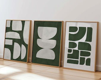 Puede incluir: Tres impresiones artísticas abstractas enmarcadas. Cada impresión presenta un diseño geométrico diferente en blanco sobre un fondo verde oscuro o blanco. Los marcos son de color madera clara y las impresiones están apoyadas contra una pared blanca.