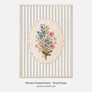 K&ouml;nnte beinhalten: Holzgerahmtes Poster mit floralem Stickmuster. Das Kunstwerk zeigt einen Strau&szlig; aus rosa, blauen und wei&szlig;en Blumen auf einem ovalen, cremefarbenen Hintergrund mit gewelltem Rand. Der Hintergrund hat vertikale blaue und wei&szlig;e Streifen. Das Poster ist 50x70cm gro&szlig;.