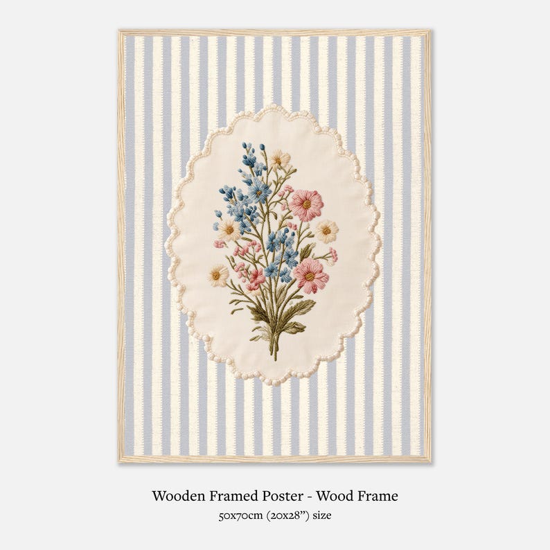 K&ouml;nnte beinhalten: Holzgerahmtes Poster mit floralem Stickmuster. Das Kunstwerk zeigt einen Strau&szlig; aus rosa, blauen und wei&szlig;en Blumen auf einem ovalen, cremefarbenen Hintergrund mit gewelltem Rand. Der Hintergrund hat vertikale blaue und wei&szlig;e Streifen. Das Poster ist 50x70cm gro&szlig;.
