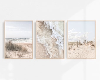 May include: Set of three framed beach photographs. The first image shows a sandy beach with a view of the ocean and a grassy dune. The second image shows a close-up of foamy waves crashing on the sand. The third image shows a path through a sandy dune with wooden posts lining the path.
