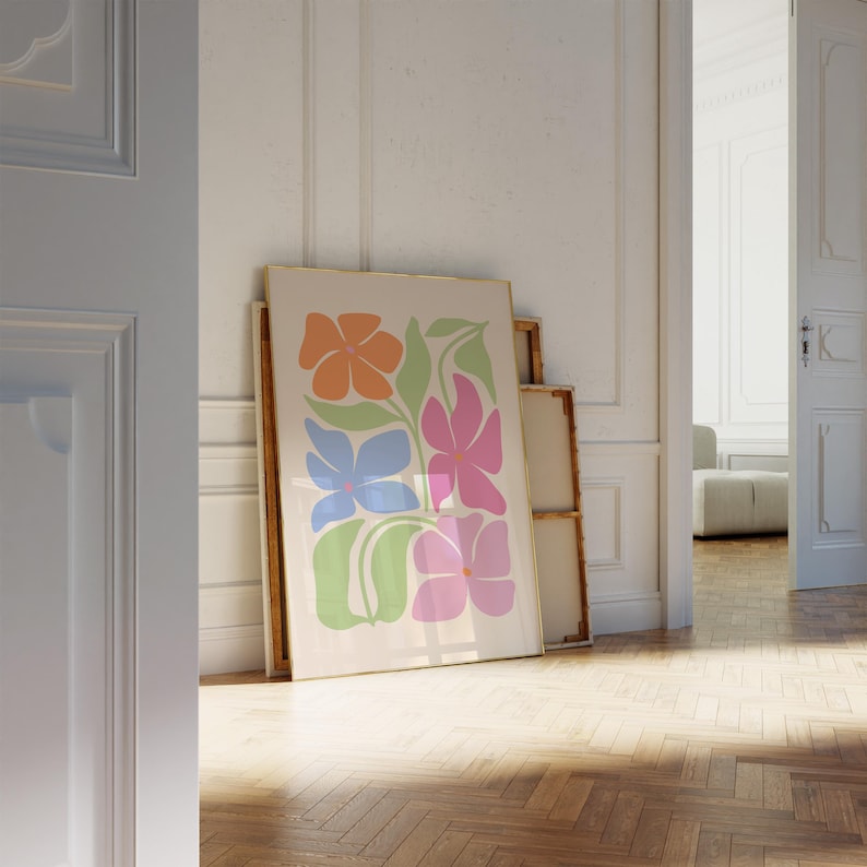 K&ouml;nnte beinhalten: Ein gerahmter Kunstdruck mit einem Blumendesign in Orange, Rosa, Blau und Gr&uuml;n. Das Kunstwerk wird vor anderen gerahmten St&uuml;cken in einem Raum mit Holzboden pr&auml;sentiert. Der Druck wird vor einem neutralen Hintergrund angezeigt.