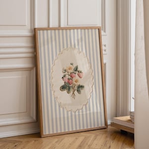 May include: A framed artwork featuring a vintage-style strawberry and flower bouquet. The artwork is set against a striped background of light blue and white. The frame is made of light-colored wood, and the artwork is leaning against a wall.