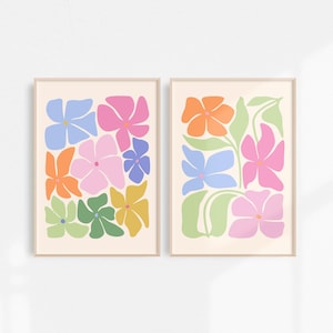 K&ouml;nnte beinhalten: Zwei gerahmte Kunstdrucke mit Blumenmotiven. Jeder Druck zeigt farbenfrohe, stilisierte Blumen in Rosa-, Orange-, Blau-, Gr&uuml;n- und Gelbt&ouml;nen auf cremefarbenem Hintergrund. Die Rahmen sind hellbeige.
