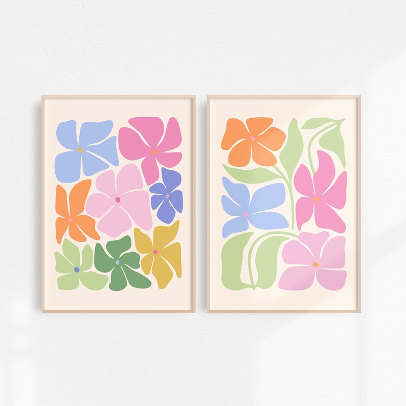 K&ouml;nnte beinhalten: Zwei gerahmte Kunstdrucke mit Blumenmotiven. Jeder Druck zeigt farbenfrohe, stilisierte Blumen in Rosa-, Orange-, Blau-, Gr&uuml;n- und Gelbt&ouml;nen auf cremefarbenem Hintergrund. Die Rahmen sind hellbeige.