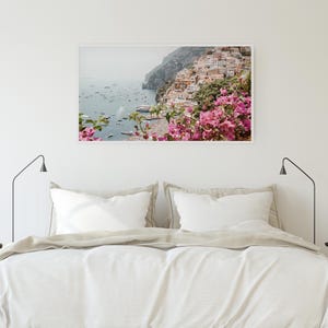 May include: A photograph of a colorful Italian village on a cliff overlooking the ocean. The village is surrounded by lush greenery and pink flowers.