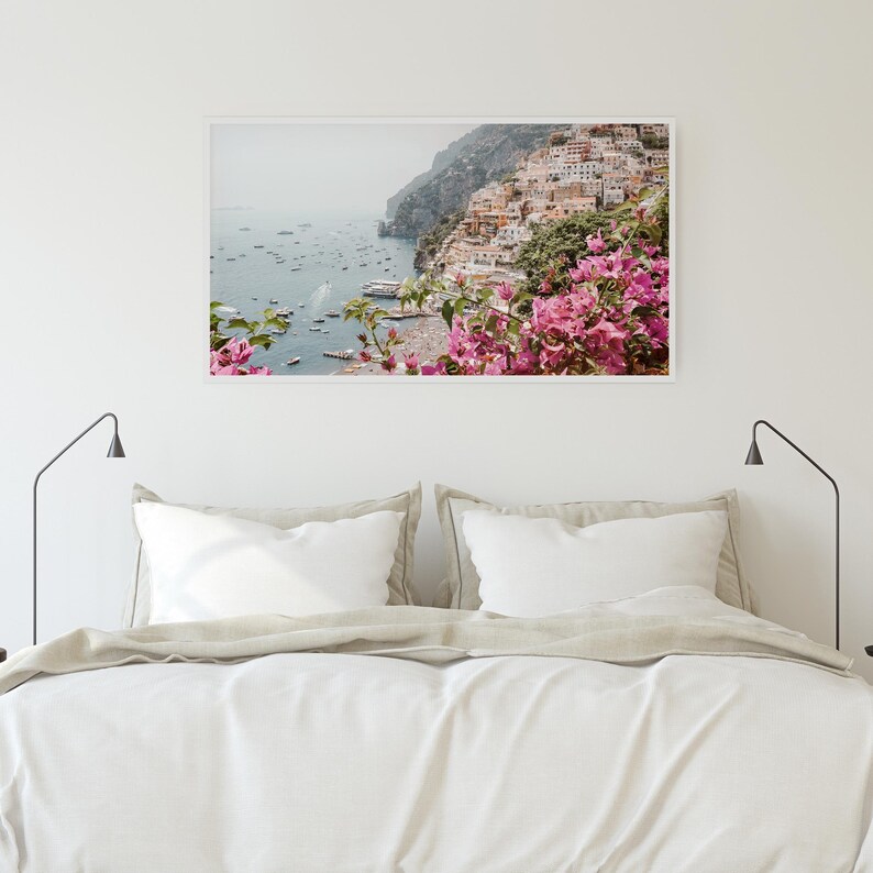 May include: A photograph of a colorful Italian village on a cliff overlooking the ocean. The village is surrounded by lush greenery and pink flowers.