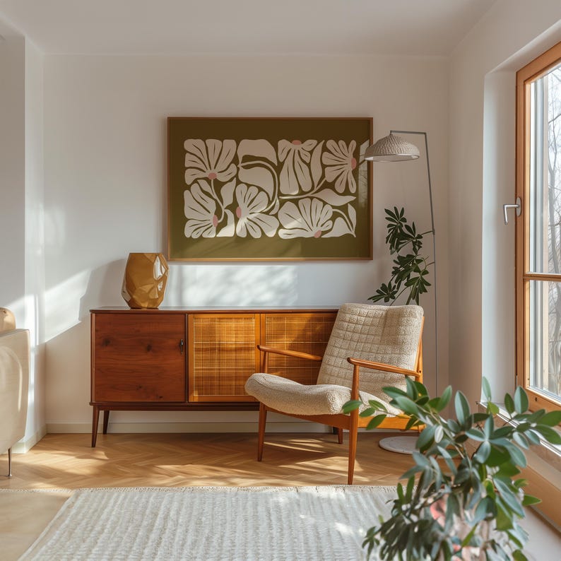 May include: A mid-century modern living room scene featuring a wooden cabinet, a beige armchair, and a framed floral print. A gold geometric vase sits atop the cabinet. A floor lamp and a potted plant add to the decor.