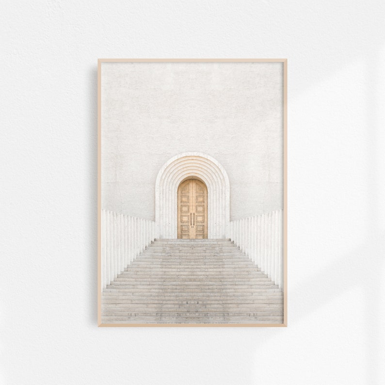 May include: A photograph of a white building with a wooden door and a set of stairs leading up to it. The door is arched and has a series of smaller arches above it.