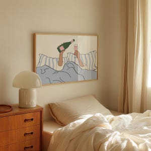 May include: A framed illustration of a person in bed with a glass of champagne and a bottle of champagne. The illustration is in a minimalist style with a light blue, white, and pink colour scheme.