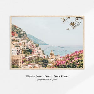 May include: A framed poster featuring a coastal Italian town with colorful buildings cascading down a hillside to the sea. The image includes a church with a dome, boats, and vibrant pink flowers. The poster is 20x28 inches.
