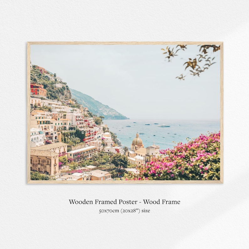 May include: A framed poster featuring a coastal Italian town with colorful buildings cascading down a hillside to the sea. The image includes a church with a dome, boats, and vibrant pink flowers. The poster is 20x28 inches.