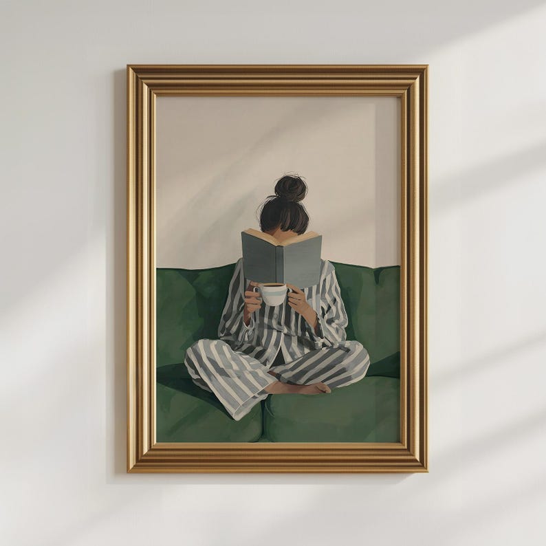 May include: Framed art print of a person in striped pajamas reading a book while seated on a green sofa. The person is holding a white cup. The artwork is in a gold frame and is against a white wall.