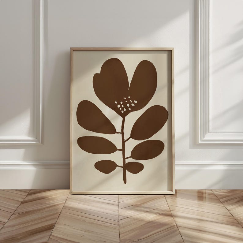 Pu&ograve; includere: Una stampa artistica incorniciata con un fiore marrone stilizzato su sfondo beige. Il fiore ha un caratteristico design a petali con dettagli a pois bianchi. La stampa &egrave; in una cornice di legno chiaro.