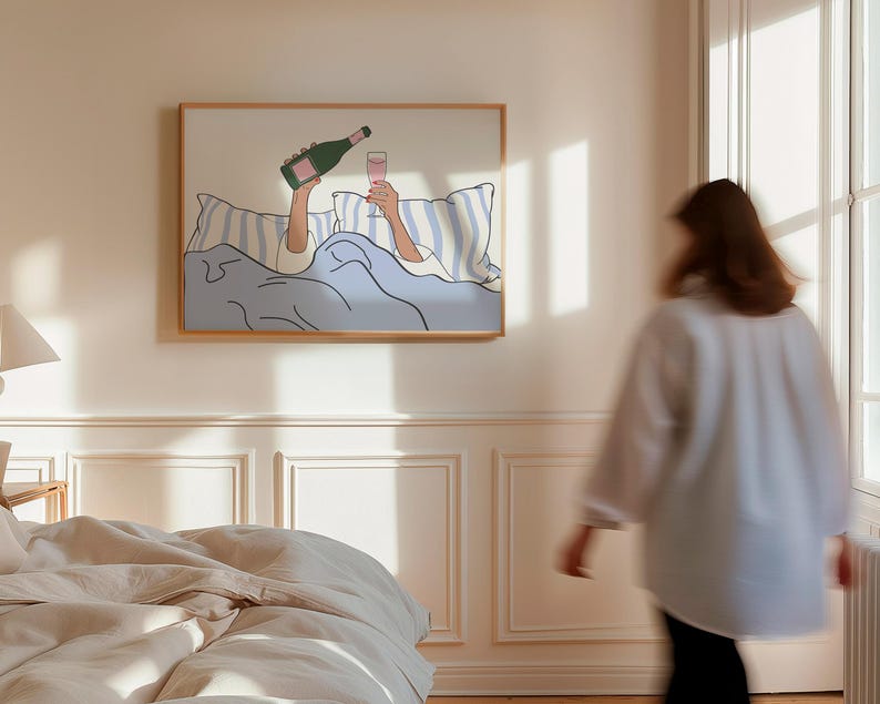 May include: A framed illustration of a person in bed with a glass of champagne and a bottle of champagne. The person is holding the glass in one hand and the bottle in the other. The illustration is in a minimalist style with a light blue background.