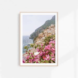 May include: A colorful photograph of a coastal town in Italy. The town is built on a steep cliffside, with buildings cascading down to the water. The photo is taken from a viewpoint overlooking the town, with a lush green hillside in the foreground. The water is a deep blue, and there are boats in the distance.