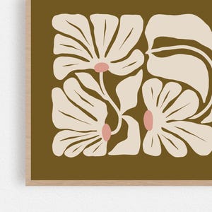 May include: Floral art print featuring stylized cream-colored flowers with pink centers and large leaves against a dark olive-green background. The artwork is framed in a light wood frame, creating a modern, minimalist aesthetic.