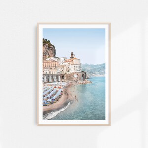 K&ouml;nnte beinhalten: Ein Foto einer K&uuml;stenstadt in Italien mit bunten Geb&auml;uden auf einer Klippe, die auf einen Sandstrand mit blauen und wei&szlig;en Sonnenschirmen blickt. Das Wasser ist klar und blau.