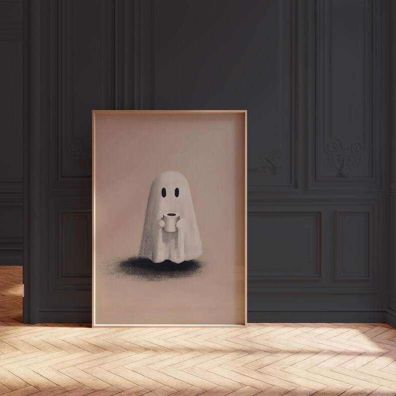 May include: A framed art print features a whimsical illustration of a ghost holding a coffee cup. The ghost is depicted in white against a light brown background, with a shadow beneath it. The frame is a light gold color.