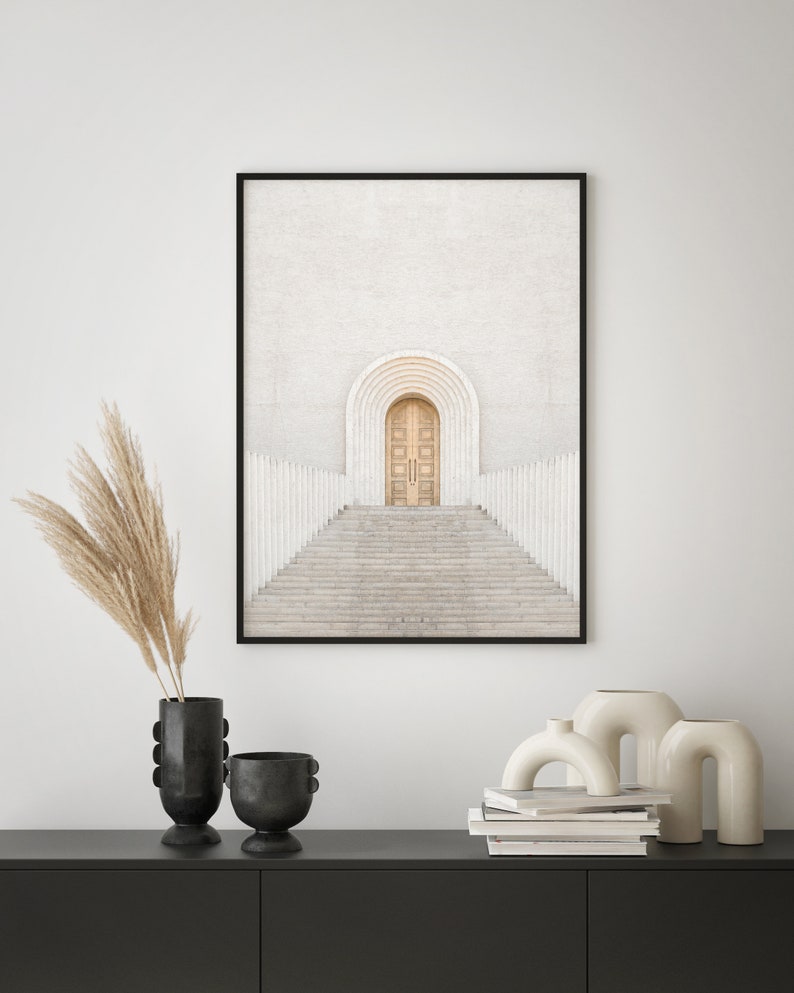 May include: A framed print of a white building with a large arched doorway and a set of stairs leading up to it. The door is a light brown wood and the building is surrounded by white columns.