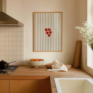 May include: A framed art print depicting a cluster of red cherries against a striped backdrop. The artwork is in a kitchen, with a wooden worktop, a bowl of oranges, and a white sink. The frame is made of wood.