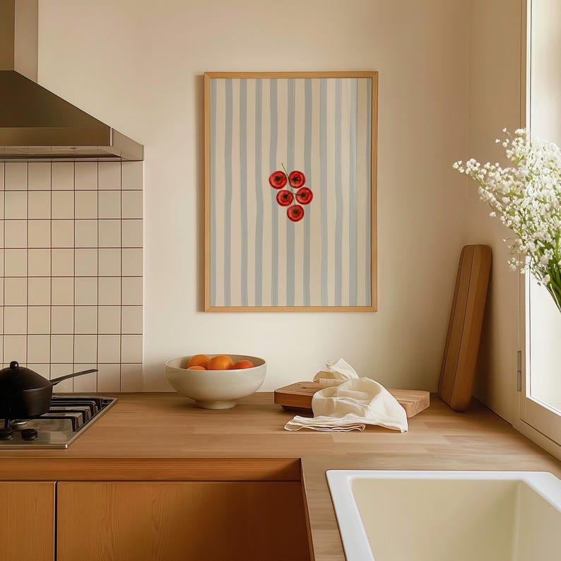 May include: A framed art print depicting a cluster of red cherries against a striped backdrop. The artwork is in a kitchen, with a wooden worktop, a bowl of oranges, and a white sink. The frame is made of wood.