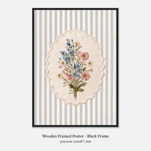 K&ouml;nnte beinhalten: Gerahmtes Poster mit einem gestickten Blumenstrau&szlig; in Rosa, Blau und Gelb. Der Strau&szlig; befindet sich auf einem cremefarbenen, gewellten Oval vor einem gestreiften Hintergrund. Der schwarze Rahmen enth&auml;lt ein 50x70cm Poster.