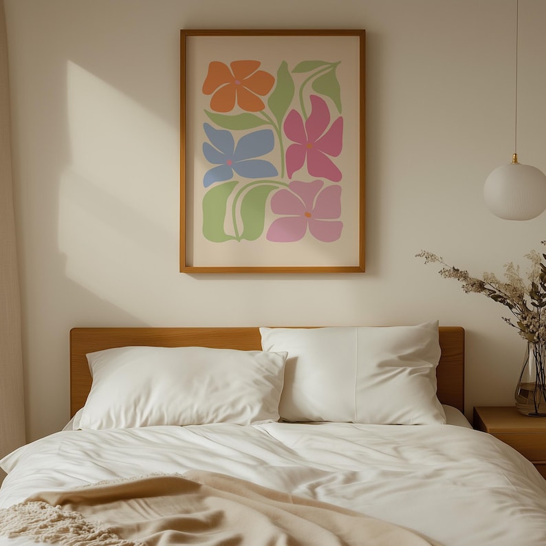 K&ouml;nnte beinhalten: Ein gerahmter Kunstdruck mit orangefarbenen, blauen und rosa Blumen und gr&uuml;nen Bl&auml;ttern. Das Kunstwerk h&auml;ngt &uuml;ber einem Bett mit wei&szlig;er Bettw&auml;sche und einem h&ouml;lzernen Kopfteil und schafft eine ruhige Schlafzimmer&auml;sthetik.