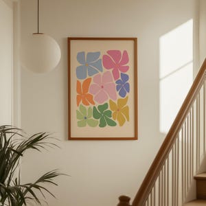 K&ouml;nnte beinhalten: Ein gerahmter Kunstdruck mit einem farbenfrohen Blumenmuster. Das Kunstwerk zeigt stilisierte Blumen in Blau-, Rosa-, Orange-, Gr&uuml;n- und Gelbt&ouml;nen auf cremefarbenem Hintergrund. Der Rahmen ist warmbraun.