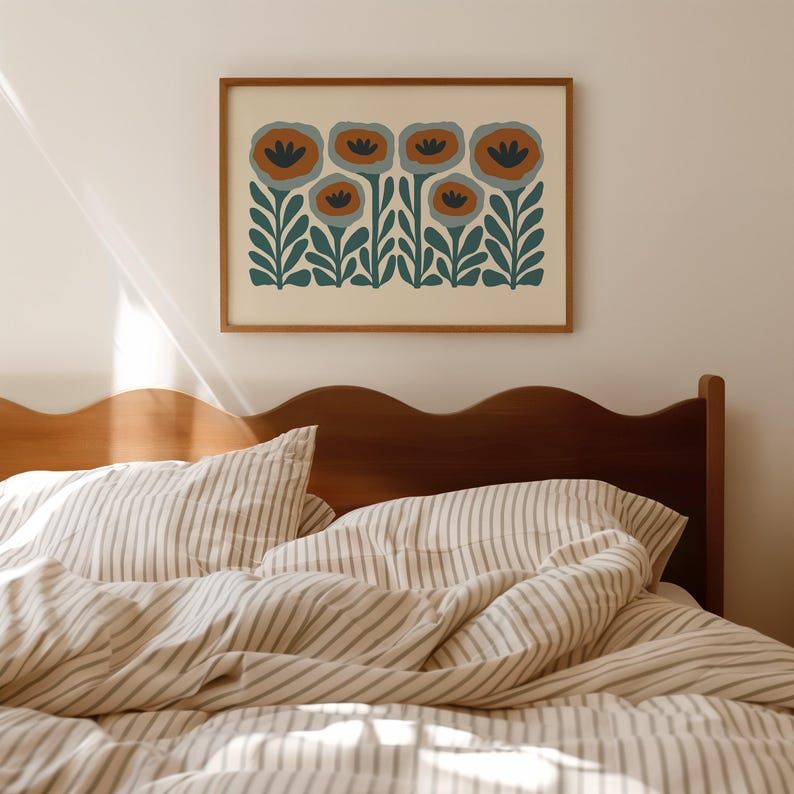 May include: A framed floral art print featuring stylized flowers in shades of orange, blue, and green. The artwork is displayed above a bed with striped bedding and a wooden headboard. The overall aesthetic is minimalist and modern.